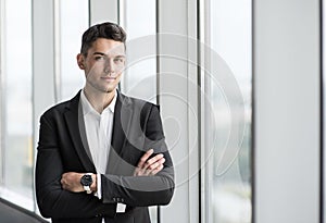 Handsome young businessman with folded arms in the office. Cheerful self confident man with crossed hands portrait