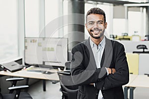 Handsome young businessman with folded arms in the office. Cheerful self confident men with crossed hands portrait. Business succe