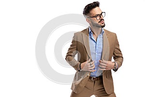 Handsome young businessman with glasses looking to side and fixing suit