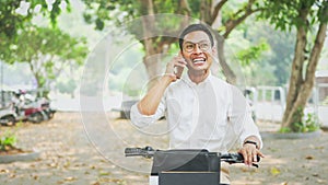 Handsome young businessman having phone call sitting on his bike at city park