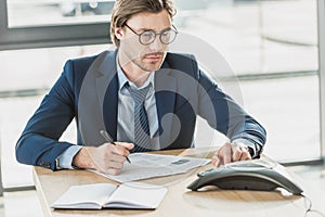 handsome young businessman with lot of paperwork using conference phone