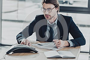 handsome young businessman with lot of paperwork using conference phone