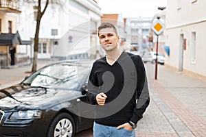 Handsome young businessman man near a black car on the street.