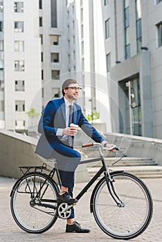 handsome young businessman with paper cup of coffee on bicycle
