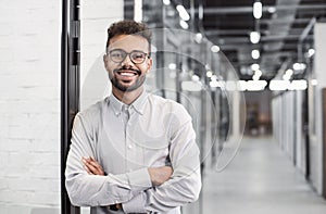 Handsome young businessman portrait. Cheerful self confident smiling man with crossed hands in office