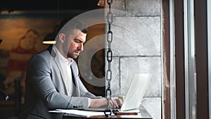 Handsome young businessman relaxing at cafe during breakfast, typing on generic laptop while checking email or messaging