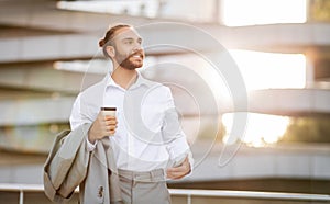 Handsome young businessman with smartphone and takeaway coffee in hands posing outdoors
