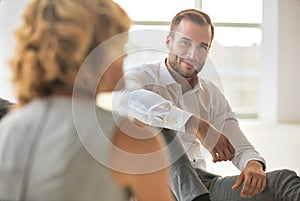 Handsome young businessman smiling while sitting on the floor with collegues in new office