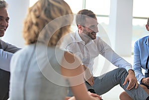 Handsome young businessman smiling while sitting on the floor with collegues in new office