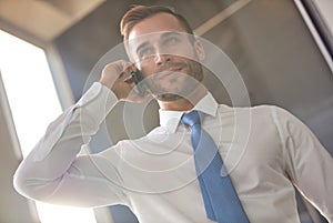 Handsome young businessman smiling while talking on smart phone while standing in new office