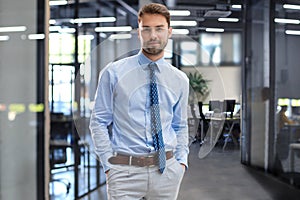 Handsome young businessman standing in modern office with collegues on the background