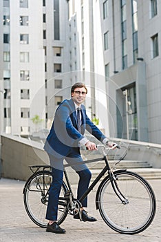 handsome young businessman in stylish suit on bicycle