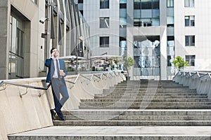 handsome young businessman in stylish suit with coffee to go talking by phone on stairs