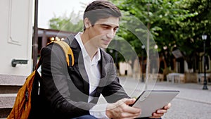 Handsome young businessman take a sit on the stairs in the middle of the street and concentrated working on his