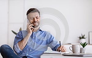 Handsome Businessman Talking On Cellphone And Taking Notes While Working In Office