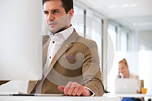Handsome young businessman using computer in office with female colleague in background