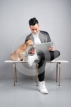 Handsome young businessman is using laptop while sitting with his dog on chair