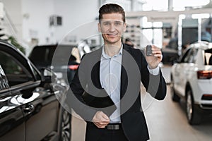 Handsome young car salesman showing car key at camera, selling autos at dealership