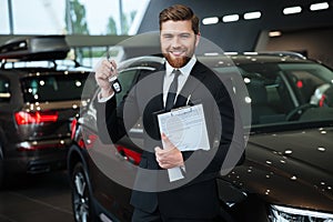 Handsome young car salesman standing at the dealership