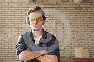 Handsome young carpenter in uniform standing in his workshop, arms crossed