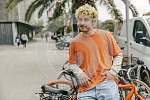 Handsome young caucasian curly guy wear orange t-shirt leaned on bicycle.