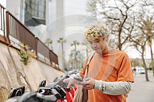 Handsome young caucasian guy using smartphone in bicycle parking lot.