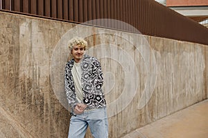 Handsome young caucasian guy wears in casual shirt stands and holds his hands in front of him.