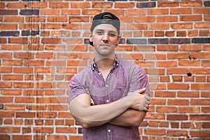 Handsome Young Caucasian Man with Cellphone and Backwards Hat Smiling for Portraits in Front of Textured Brick Wall Outside