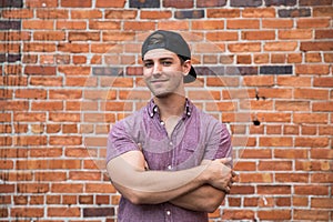 Handsome Young Caucasian Man with Cellphone and Backwards Hat Smiling for Portraits in Front of Textured Brick Wall Outside
