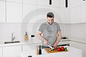 Handsome young caucasian man cooking a nice healthy vegetable meal or salad in a modern bright white kitchen