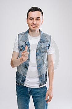 Handsome young Caucasian man in denim clothes pointing his finger at you