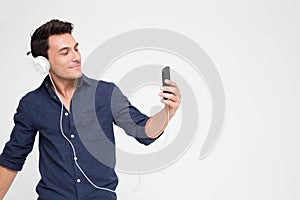 Handsome young Caucasian man listening music with headphones on smartphone,