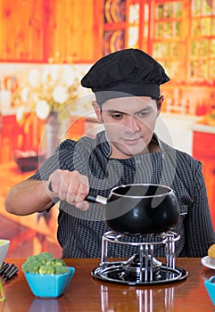 Handsome young cheff preparing a gourmet Swiss fondue dinner with assorted cheeses and a heated pot of cheese fondue and