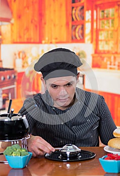 Handsome young cheff preparing a gourmet Swiss fondue dinner on wooden table in kitchen background