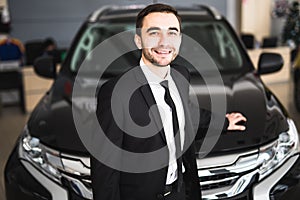 Handsome young classic car salesman standing at the dealership in front of new car