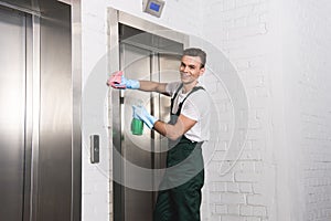 handsome young cleaner washing elevator and smiling