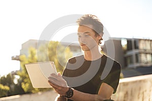 Handsome young college student using digital tablet on sunny day