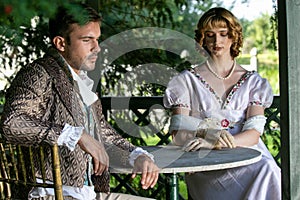 Handsome young couple in vintage clothing sit in gazebo deep in thought.