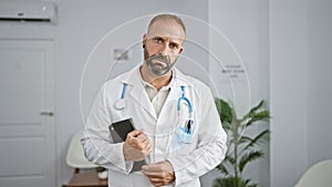 Handsome young doctor with serious face, holding a touchpad in clinic\'s waiting room while working