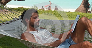 Handsome young erudite Caucasian man on vacation, relaxing outdoors, lying in a hammock over the beautiful tropical