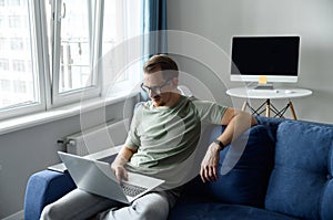 Handsome young European man with beard sitting on the sofa with laptop