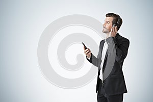 Handsome young European man smiling and listening to music or podcast with his smartphone and headphones over light gradient wall