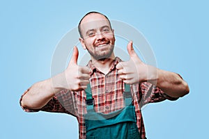 handsome young farmer with a big smile and a thumb up is captured wearing overalls in a studio shot