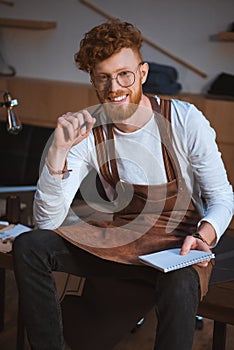 handsome young fashion designer in eyeglasses holding pencil with notebook and smiling