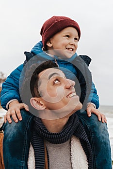 Handsome young father carrying on shoulders his little cute son while spending fun time together on beautiful beach