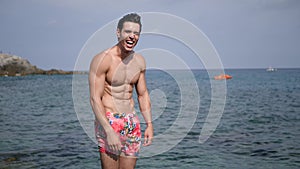 Handsome young fit man, bursting into laughter, with sea behind, large copyspace