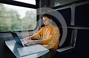 Handsome young freelancer man working on laptop in train sitting at the table. The guy uses a laptop while traveling by train