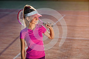 Young girl in stylish cap and sportswear with racket on shoulder on the sunshine background. Female tennis player on
