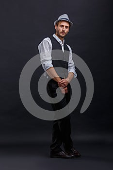 A handsome guy in a retro suit and hat, standing with arms and legs crossed.