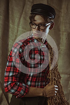 Handsome young guy in a cap and checkered shirt is holding a wild flower in his hand